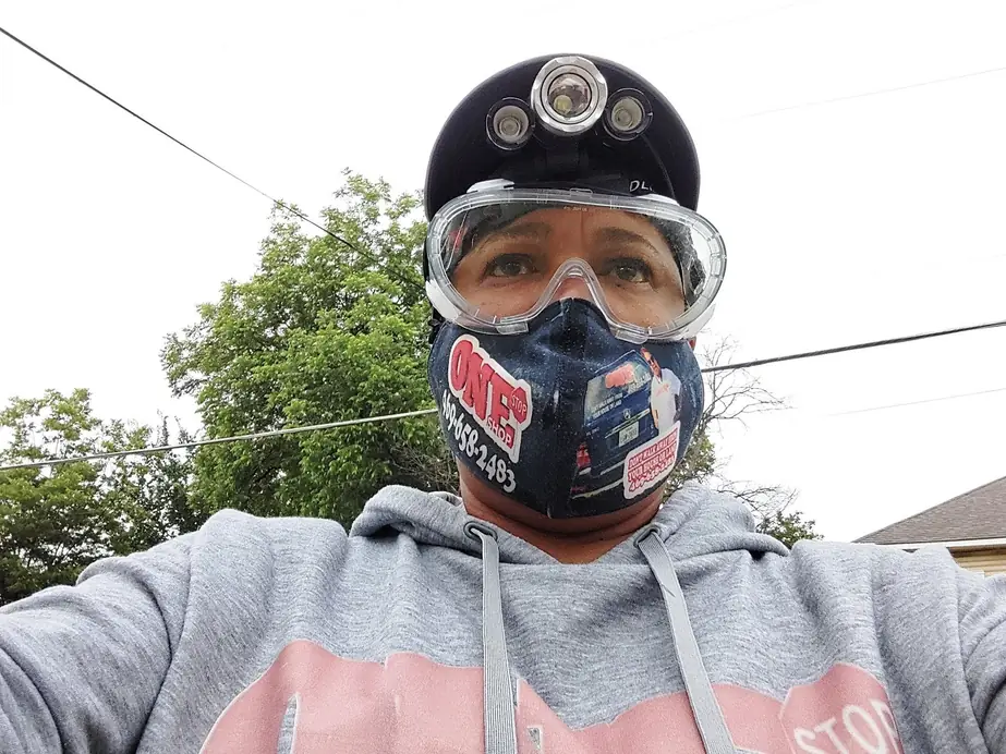 A One Stop Shop inspector in a hard hat with a headlamp, safety goggles and a respirator mask printed with the company logo